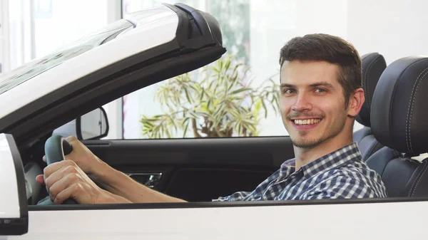 Glücklicher junger gutaussehender Mann sitzt in einem neuen Cabrio im Autohaus — Stockfoto