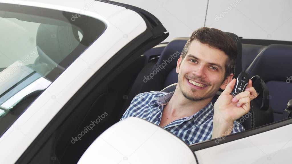 Handsome happy young male driver holding car keys sitting in his auto