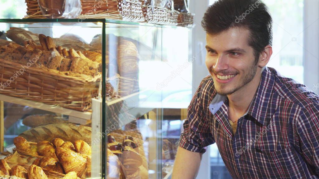 Handsome man choosing desserts from the showcase at the bakery