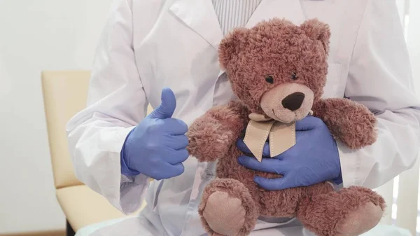 Dokter profesional memegang boneka beruang dan menunjukkan jempol ke atas — Stok Foto