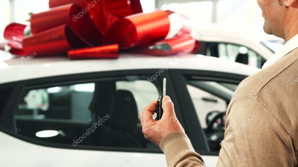 A satisfied man looks at his new car and shows the key to it