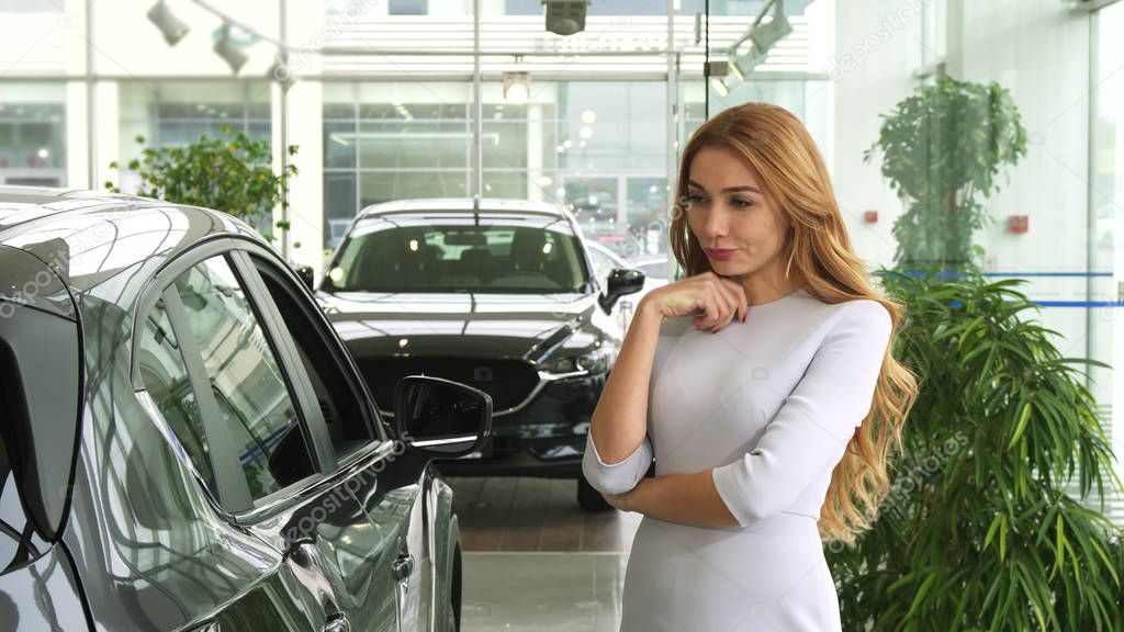 Female customer looking at the new car thoughtfully choosing auto at the dealership