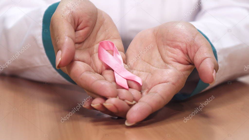 Close up of a female doctor holding pink ribbon for breast cancer awareness