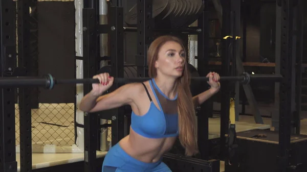 Mujer atlética joven haciendo sentadillas con una barra de ejercicio en el gimnasio — Foto de Stock