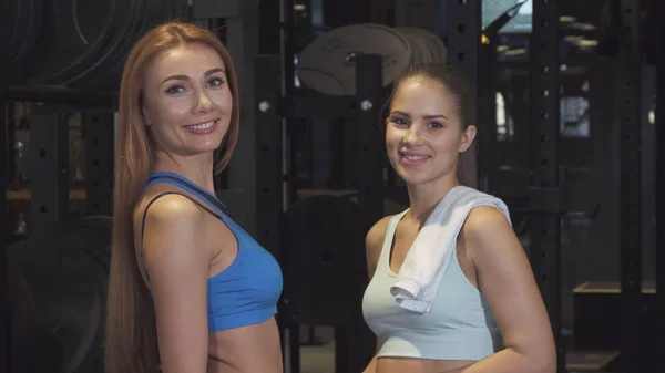 Belas mulheres atléticas jovens sorrindo para a câmera posando no ginásio — Fotografia de Stock