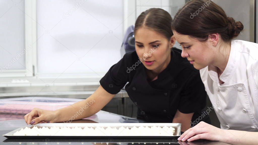 Two female confectioners examining meringues on a tray 