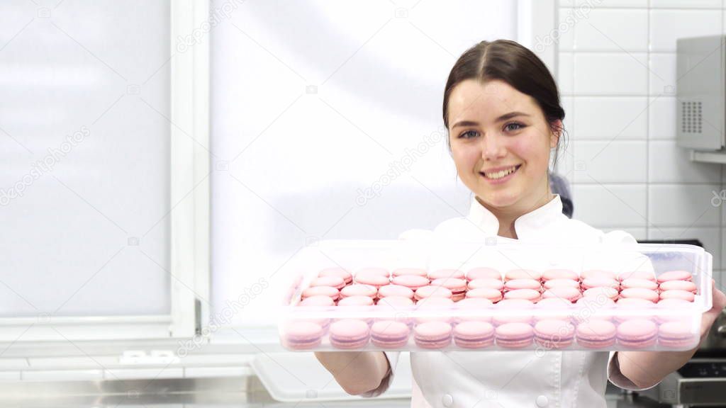 Professional confectioner smiling holding out tray full of macaroons to the camera