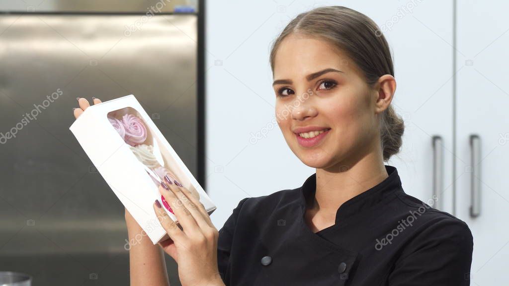 Attractive female baker smiling to the camera holding a bow of marshmallows