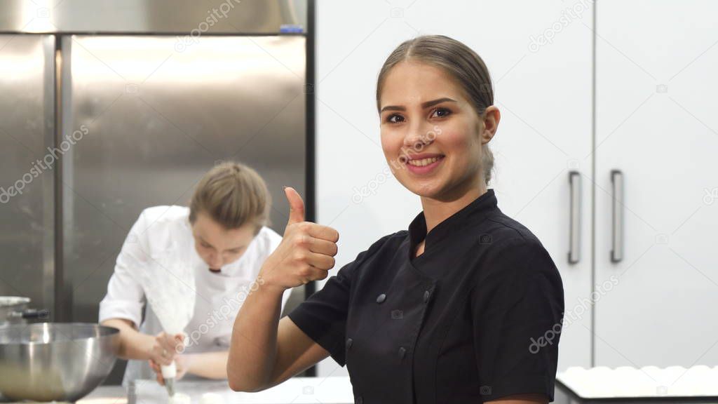 Happy female chef smiling showing thumbs up at the kitchen