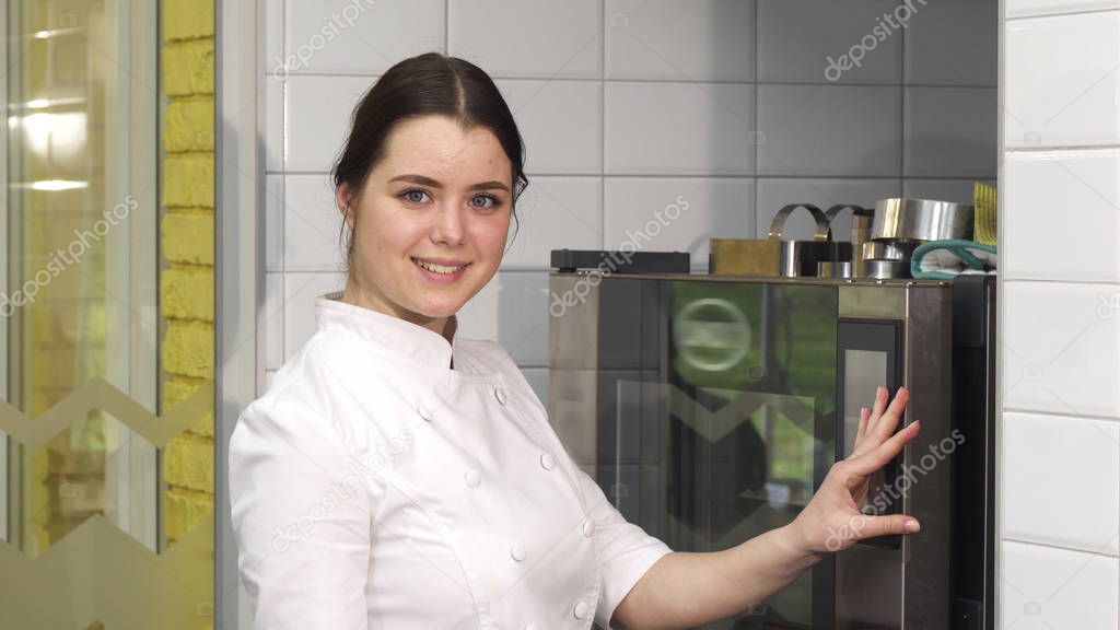 Young beautiful female confectioner putting merengues into the oven