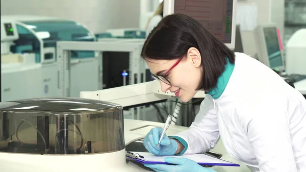 Jovem química do sexo feminino tomando notas no laboratório moderno — Fotografia de Stock