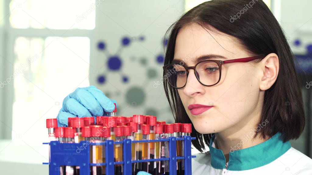 Young female researcher examining test tubes with blood samples