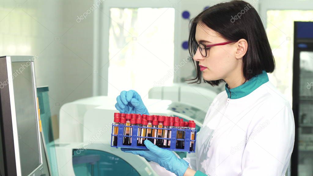 Young female scientist examining test tubes with blood samples