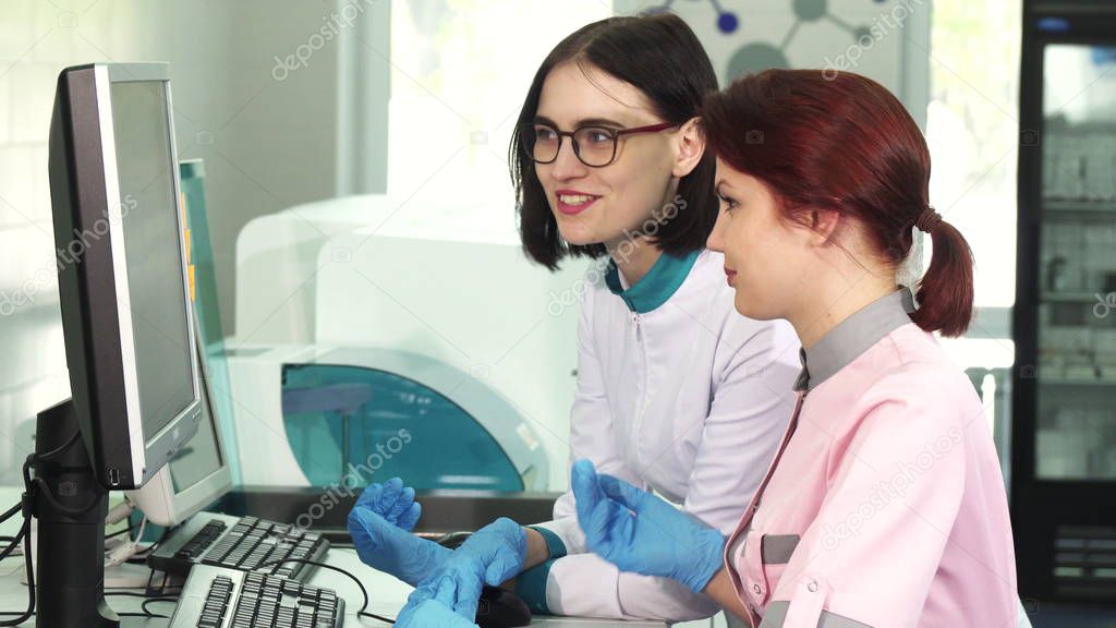 Two female lab workers operating analysing machines using computer