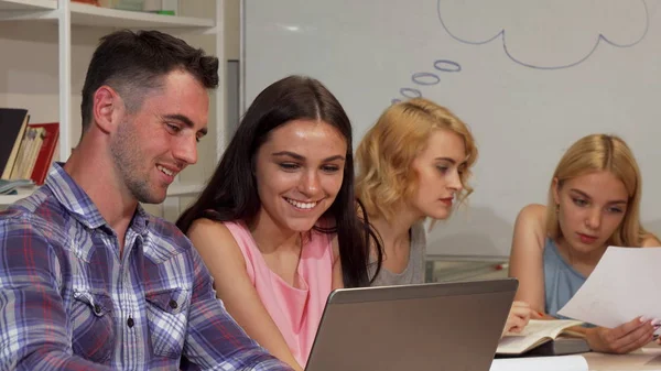 Twee jonge vrolijke studenten hun project bespreken op de laptop — Stockfoto