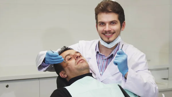 Młody mężczyzna dentysta uśmiechający się podczas dentystyczna jego pacjenta — Zdjęcie stockowe