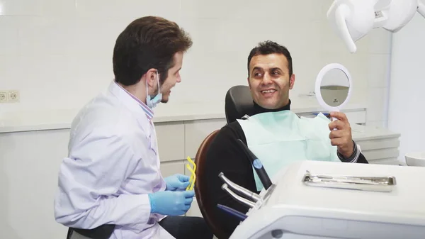 Zahnarzt gibt seinem Patienten nach der Zahnbehandlung einen Spiegel — Stockfoto