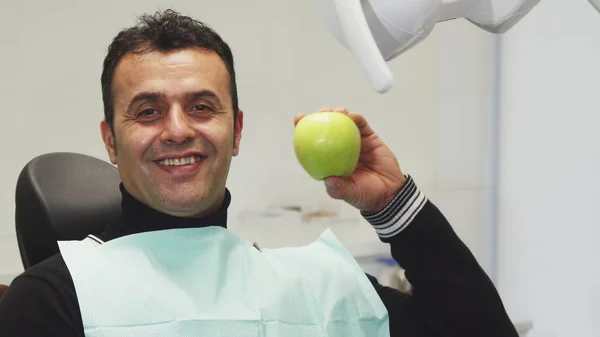 Gelukkig volwassen man die lacht een appel zit in een tandheelkundige stoel te houden — Stockfoto