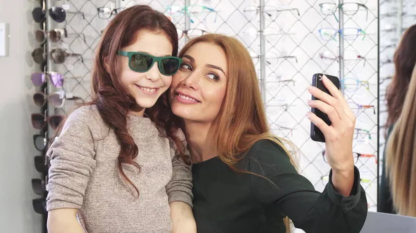 Hermosa mujer tomando selfies con su linda hija en la tienda de gafas — Foto de Stock