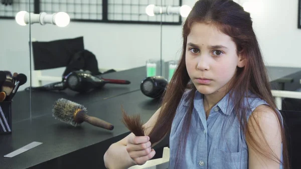 Küçük şirin kız üzgün zarar görmüş saçları split uçları ile inceleyerek arıyorsunuz