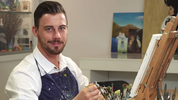 Bonito artista alegre barbudo sorrindo para a câmera enquanto trabalhava em seu estúdio — Fotografia de Stock