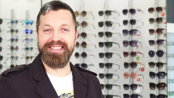 Веселый взрослый мужчина улыбается в камеру, покупая солнечные очки — стоковое фото