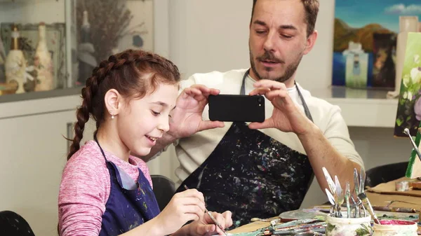 Pai feliz tirando fotos de sua filhinha fofa enquanto ela está desenhando — Fotografia de Stock