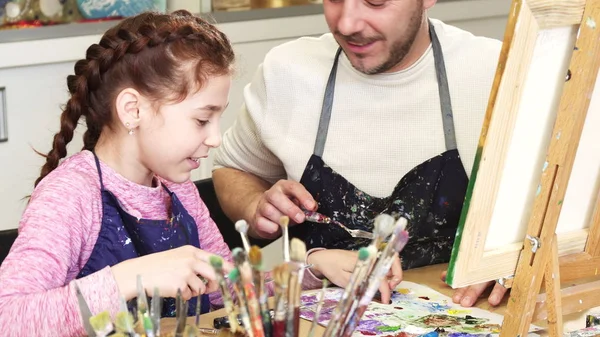 Cortada tiro de uma linda menina sorrindo falando com seu pai misturando tintas na aula de arte — Fotografia de Stock