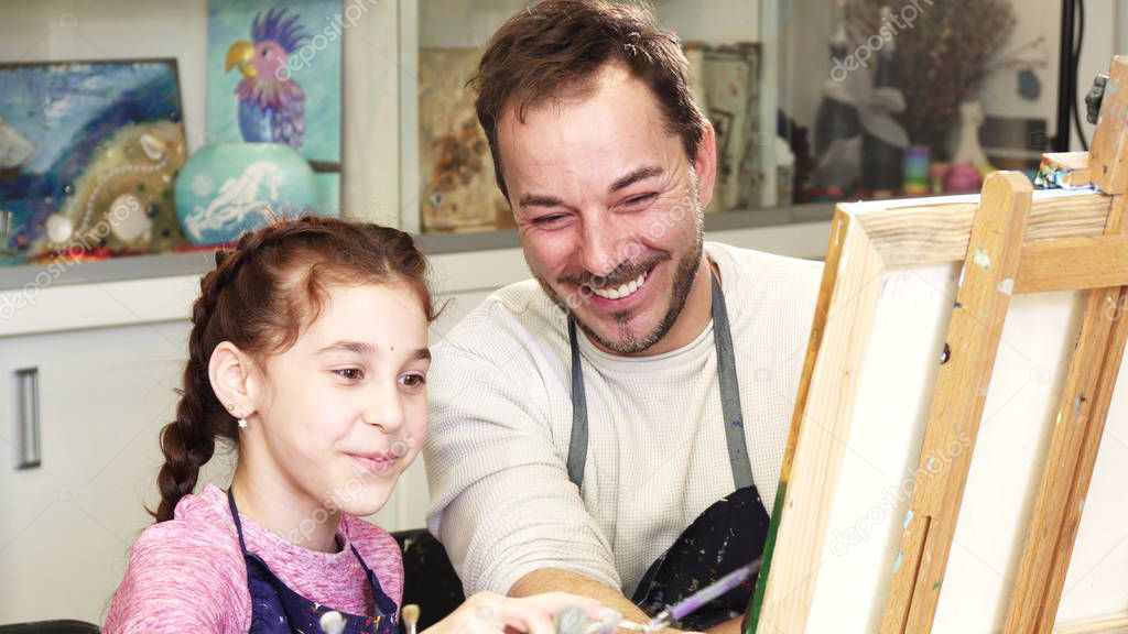 Little adorable girl and her loving father painting a picture together. Mature handsome man enjoying drawing with his young daughter family artistry artist lifestyle love creativity.