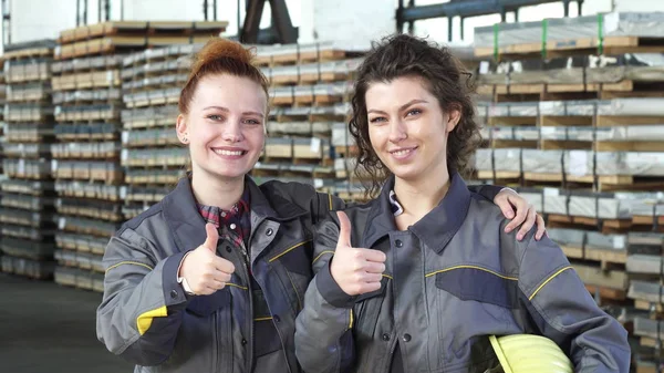 İki mutlu kadın fabrika işçilerini gösteren başparmak depolama vasıl kucaklayan