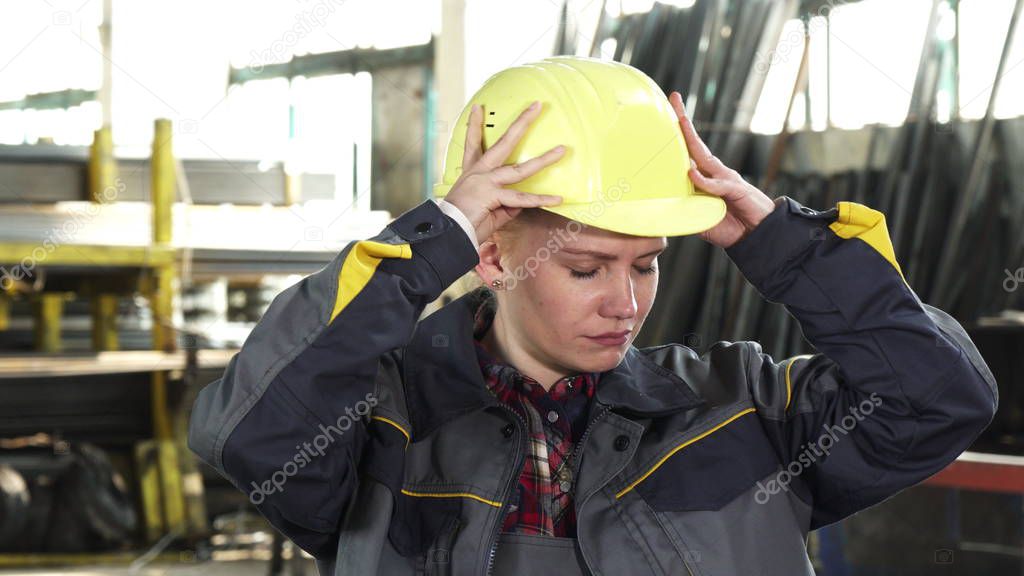 Tired female factory worker taking off her hardhat after work