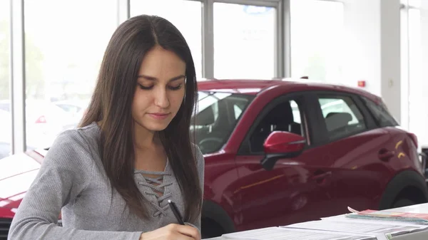Junge attraktive Fahrerin füllt Papiere im Autohaus aus — Stockfoto
