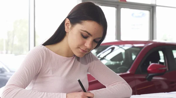 Schöne junge Frau signiert Papiere im Autohaus Showroom — Stockfoto