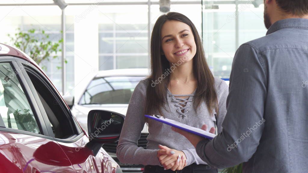 Young woman talking to the salesman at the car dealership