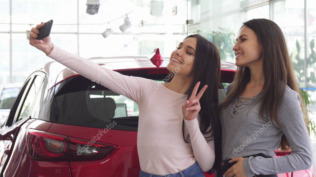 Cheerful female friends taking selfies near the new car 