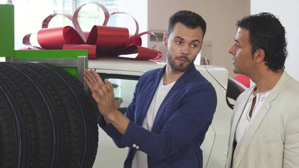 車のタイヤを選択する彼の成熟の顧客を助ける若いセールスマン — ストック写真