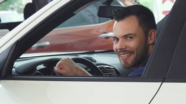 Alegre joven guapo hombre sonriendo a la cámara sentado en su nuevo coche — Foto de Stock