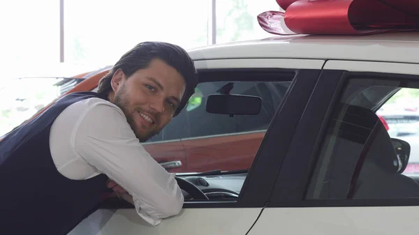 Schöner Mann lächelt in die Kamera, während er ein neues Auto begutachtet — Stockfoto