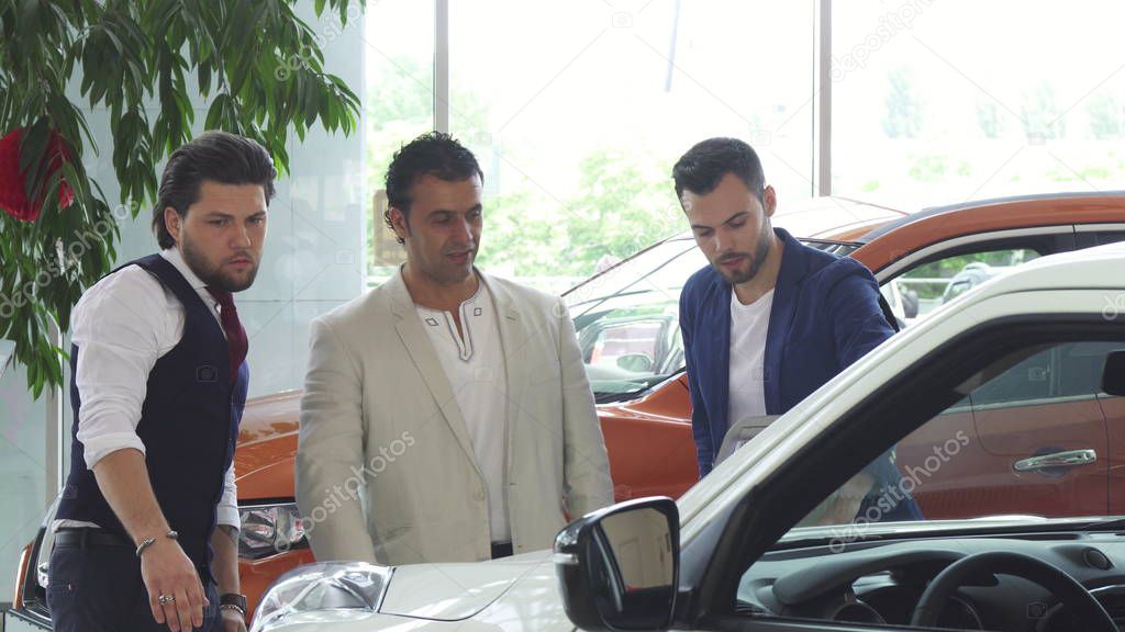 Three male friends examining car for sale at the dealership