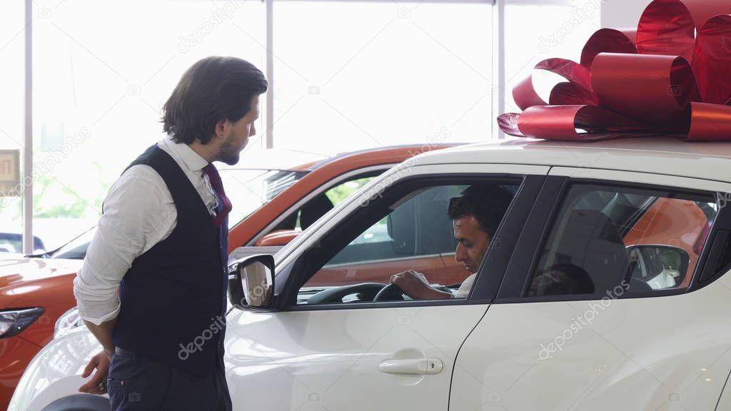 Professional car salesman opening door of a car for his male customer