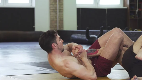 Shirtless athletic mma fighter doing armlock, while grappling at the gym