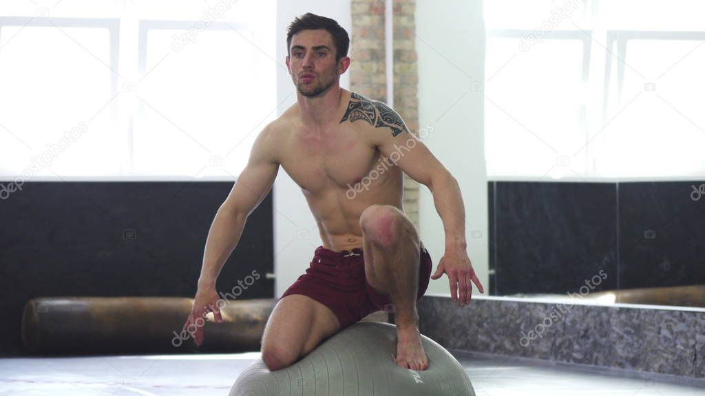 Young handsome ripped male athlete balancing on a fitness ball