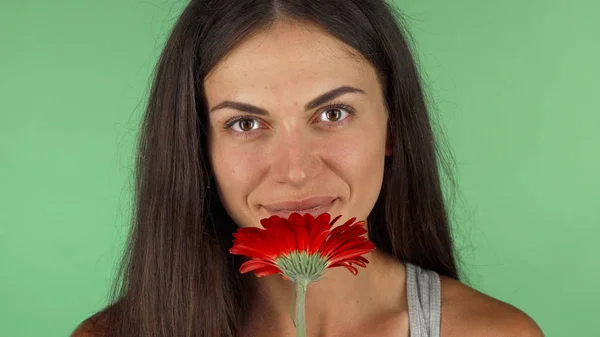 Νεαρή όμορφη γυναίκα μυρίζοντας κόκκινο λουλούδι σε chromakey πράσινο φόντο — Φωτογραφία Αρχείου