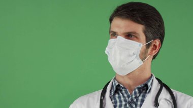 Kameraya gülümseyen bir tıbbi maske içinde neşeli erkek doktor