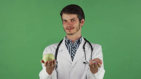Молодий лікар тримає зелене яблуко і купу таблеток — стокове фото