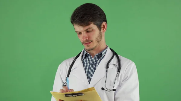 Jeune médecin masculin écrit sur son presse-papiers sur chromakey vert — Photo