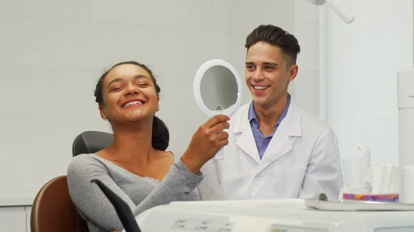 Schöne Frau überprüft ihr Lächeln im Spiegel in der Zahnklinik — Stockfoto