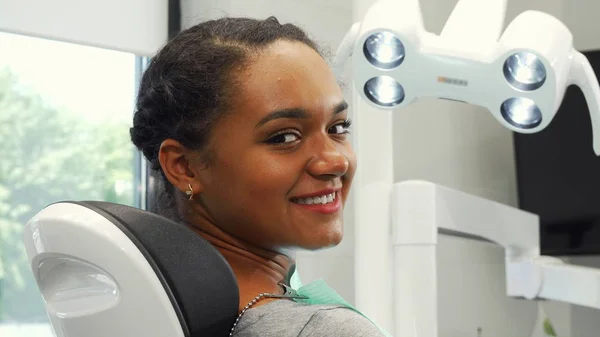 Paciente feminina atraente sorrindo para a câmera sentada em uma cadeira dentária — Fotografia de Stock