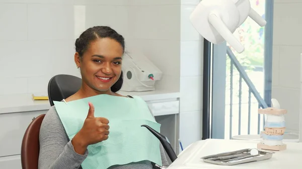 Junge Frau lächelt und zeigt Daumen hoch beim Warten auf Zahnuntersuchung — Stockfoto