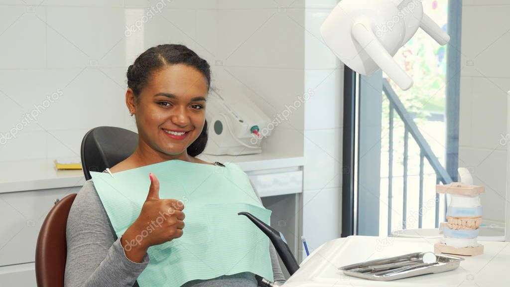Young woman smiling showing thumbs up waiting for dental checkup